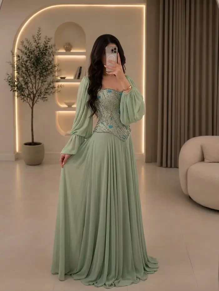 Robe de demoiselle d'honneur pour mariage au jardin à Dubaï, style henné | Robe en mousseline de soie vert sauge, épaules dénudées, manches longues bouffantes, ornée de cristaux bleus cousus main